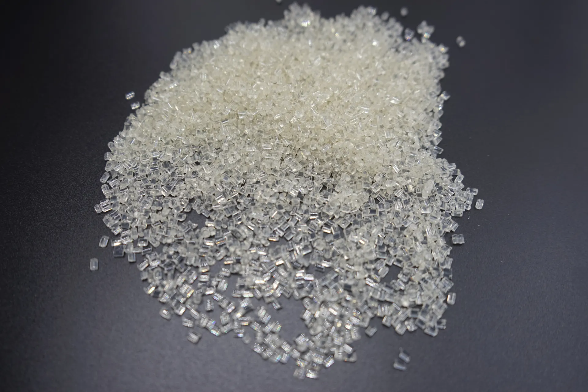 Clear plastic pellets arranged in a pile on a dark surface