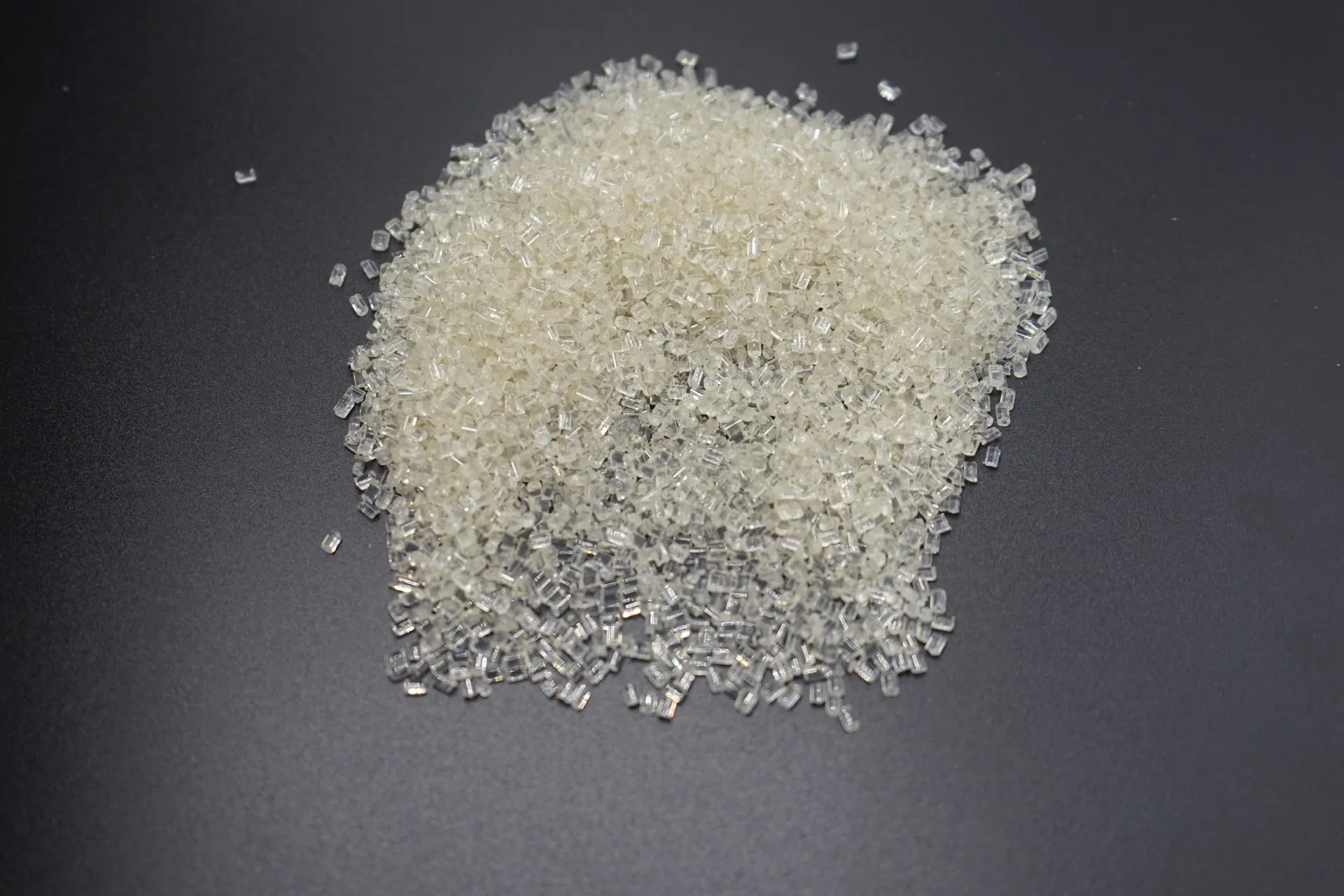 Clear plastic pellets arranged in a pile on a dark surface
