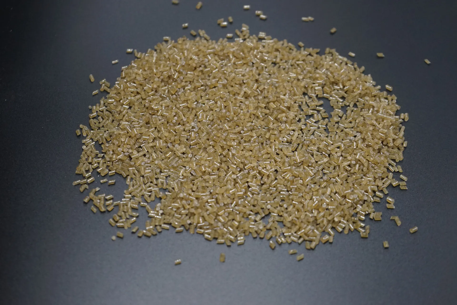 Light amber plastic pellets arranged in a pile on a dark surface