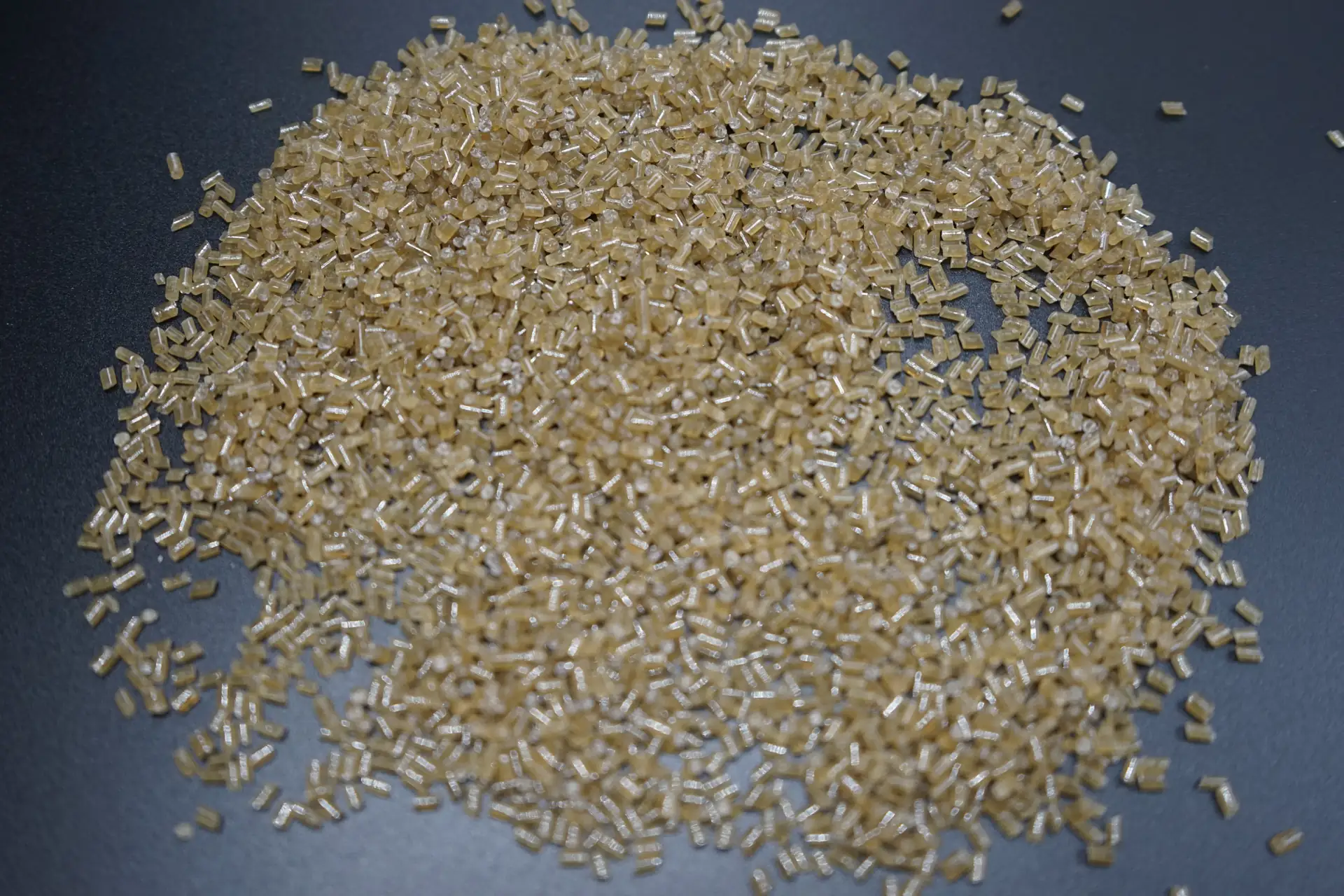 Close view of light amber plastic pellets on a dark surface