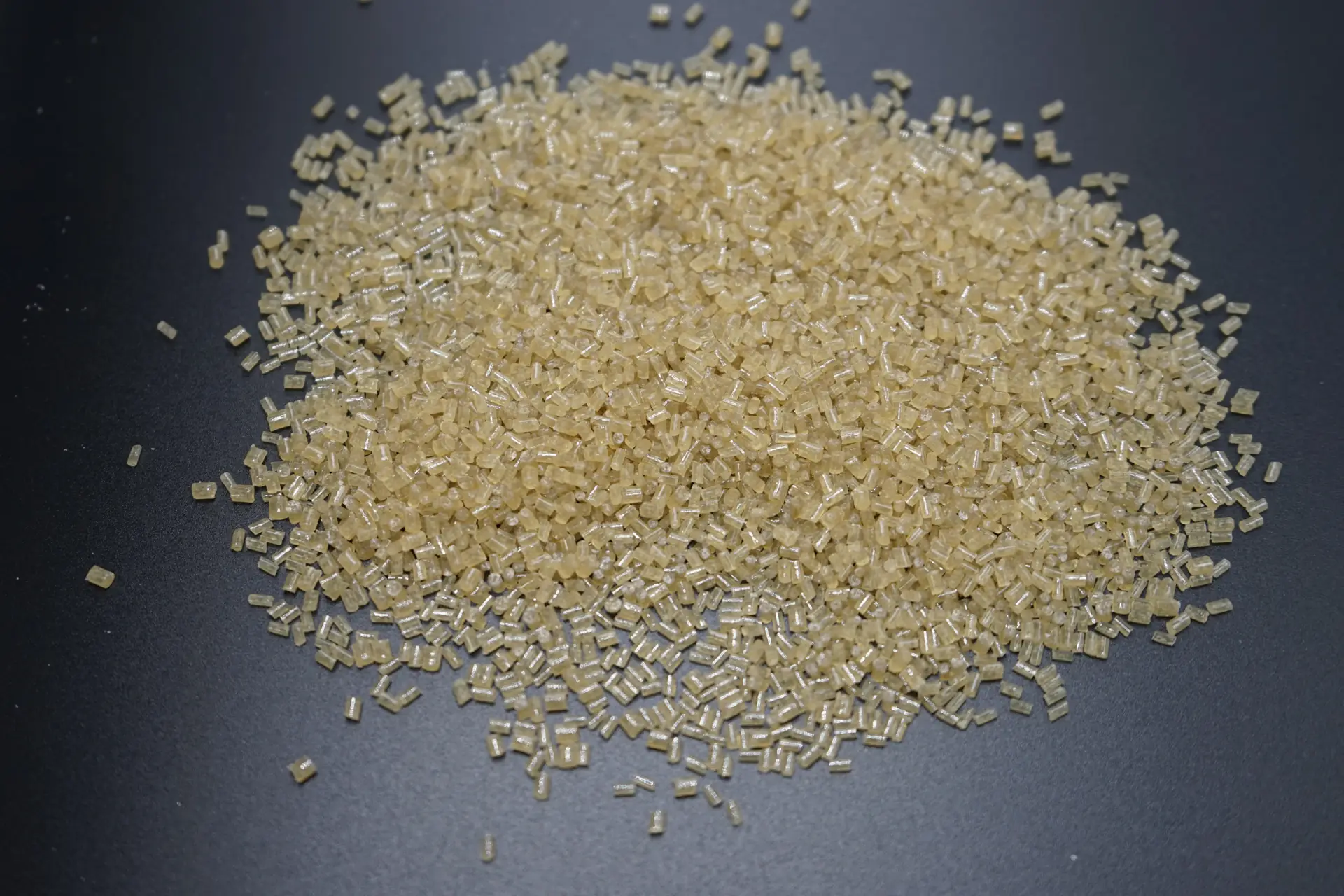 Light amber plastic pellets arranged in a pile on a dark surface