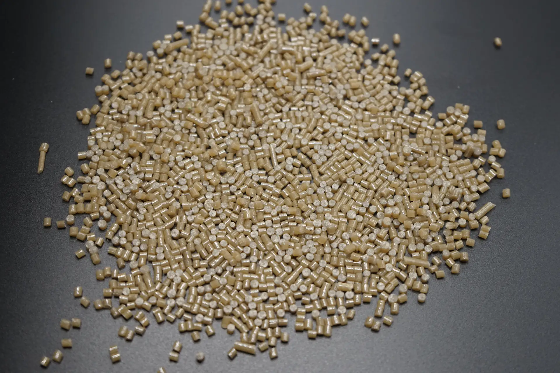 Beige plastic pellets arranged in a pile on a dark surface