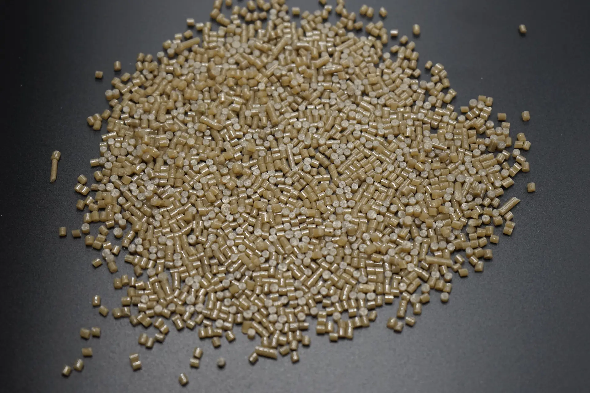 Beige plastic pellets viewed from above on a dark surface