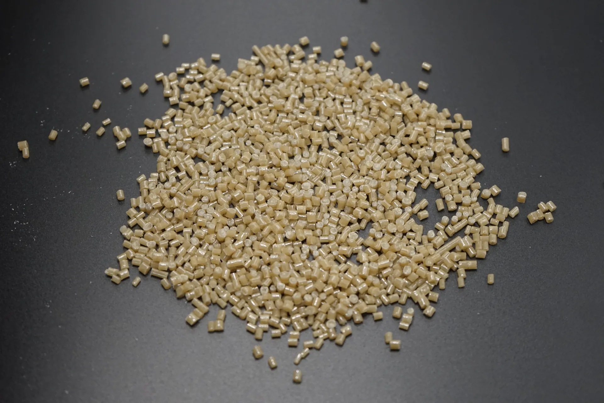 Pale amber plastic pellets arranged in a pile on a dark surface