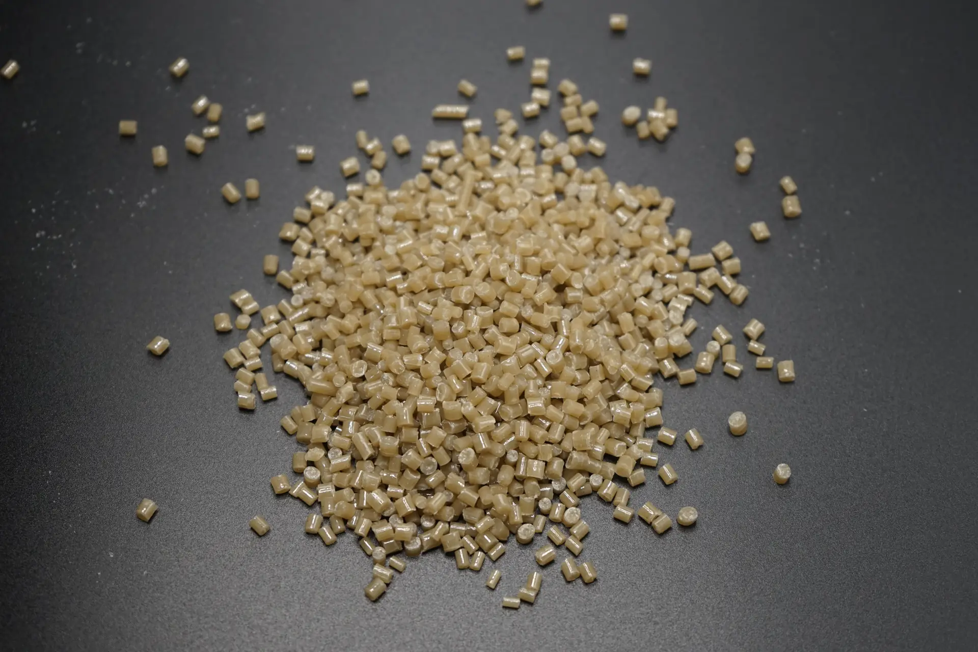 Pale amber plastic pellets arranged in a pile on a dark surface