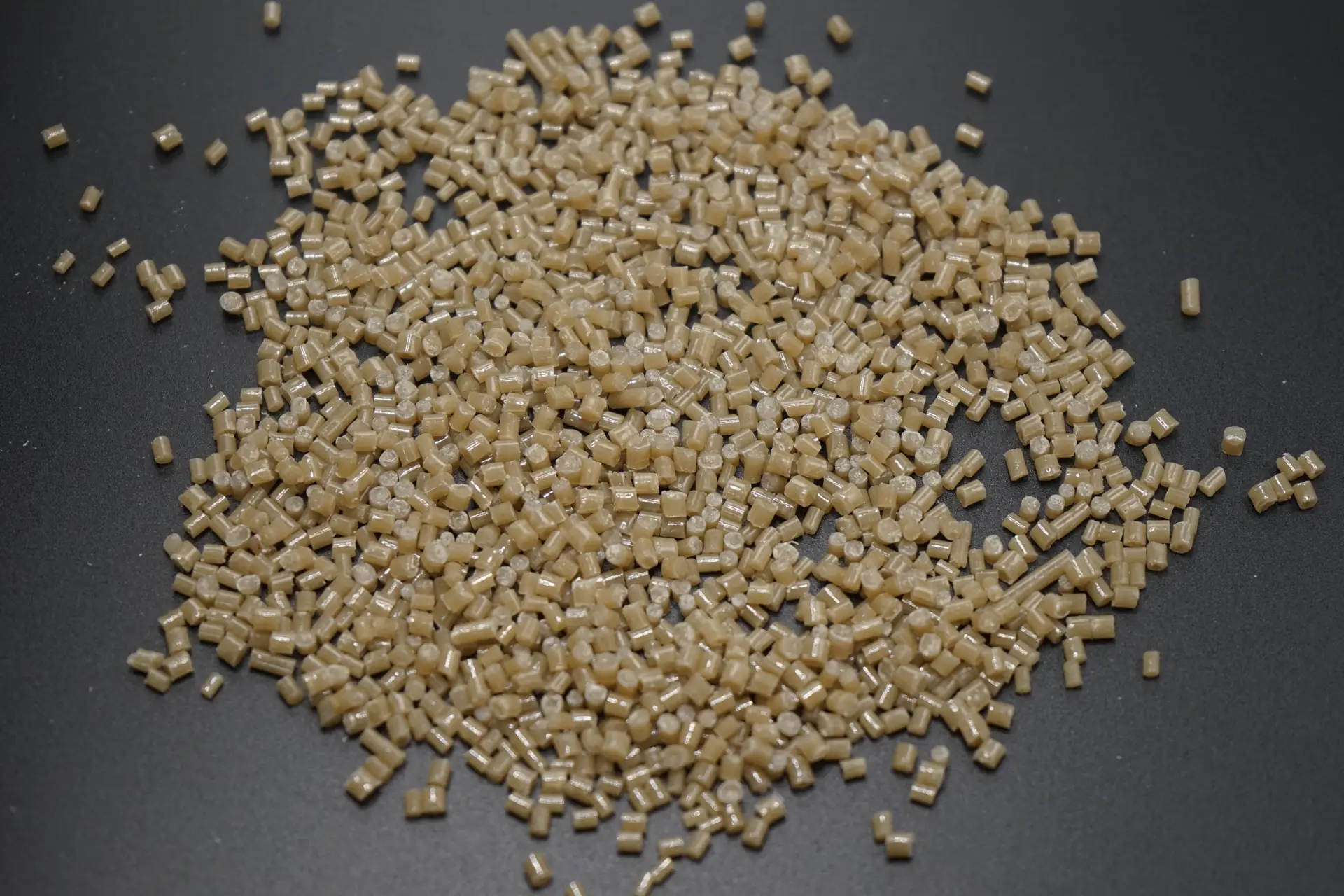 Close view of pale amber plastic pellets on a dark surface