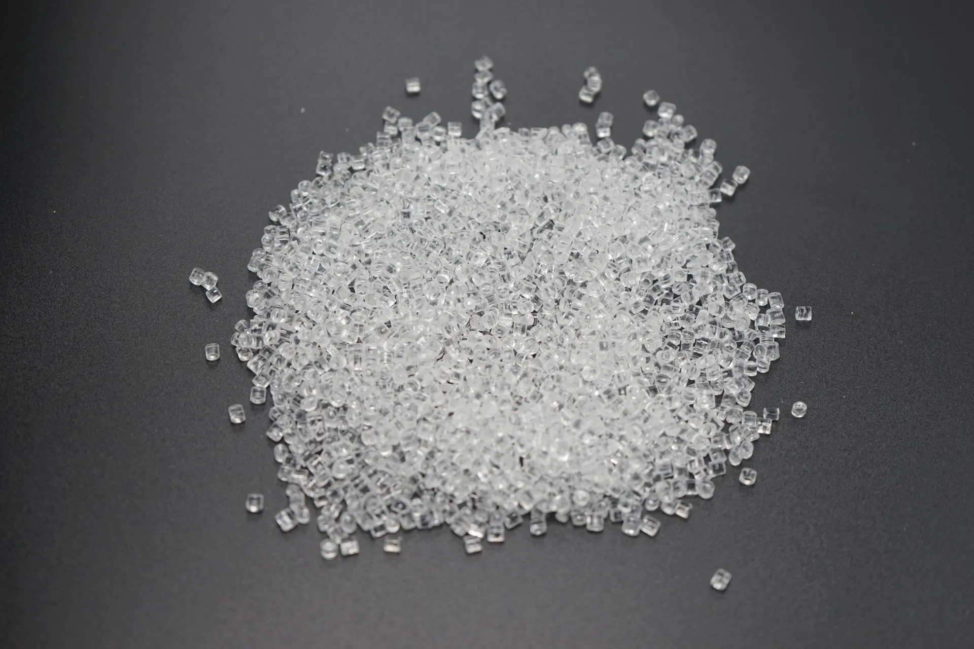 Clear plastic pellets arranged in a pile on a dark surface